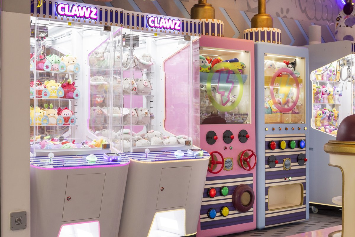 Clawz claw machines up close — pink and blue control panels, curated plush stocked inside, the same machines we bring to your event